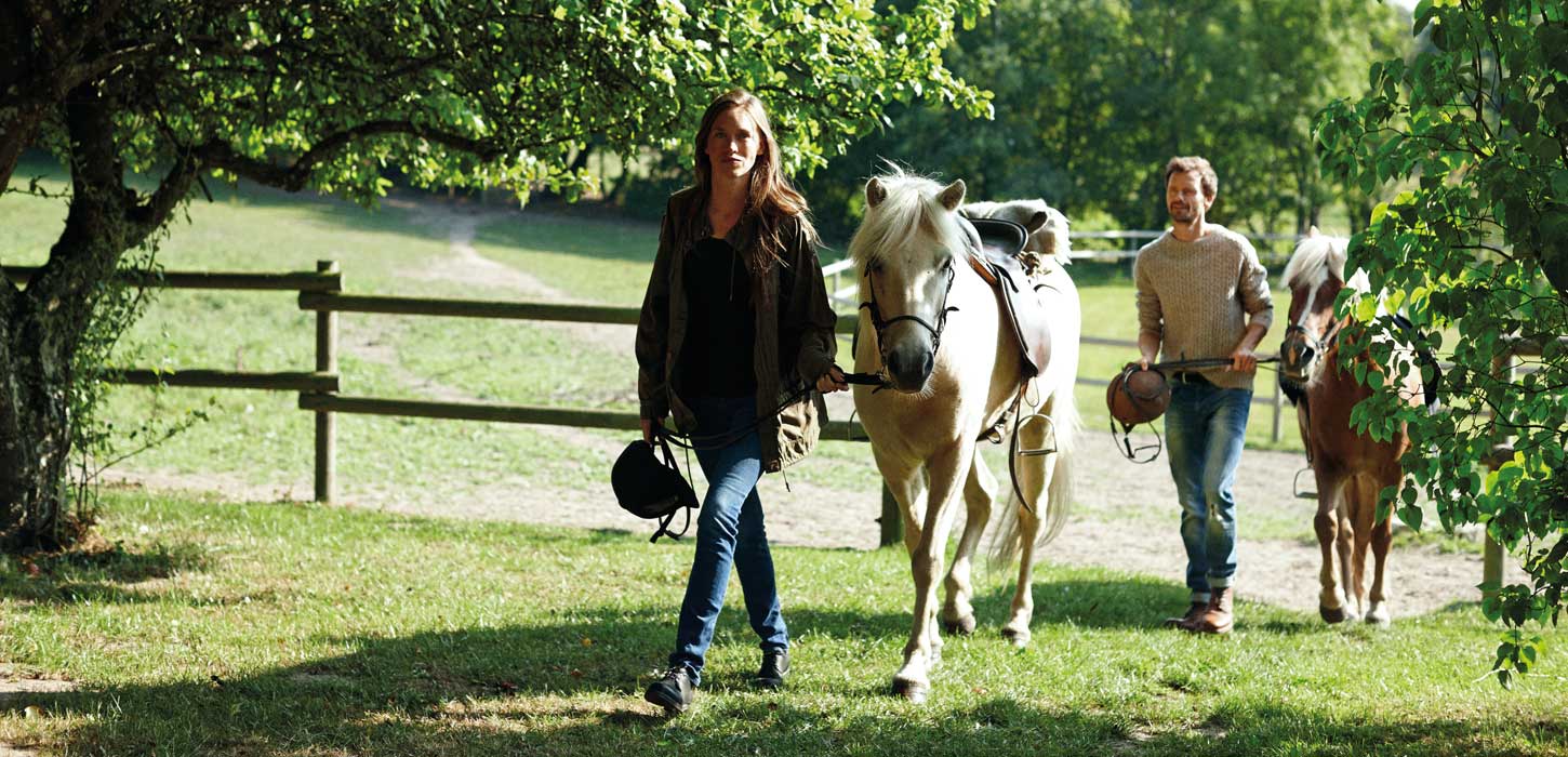 To personer går med heste ved indhegning
