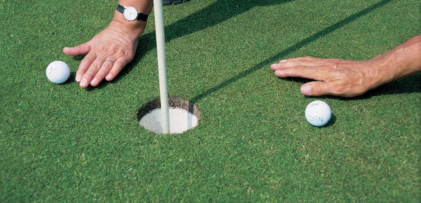 To hænder med golfbolde ved et hul på en golfbane