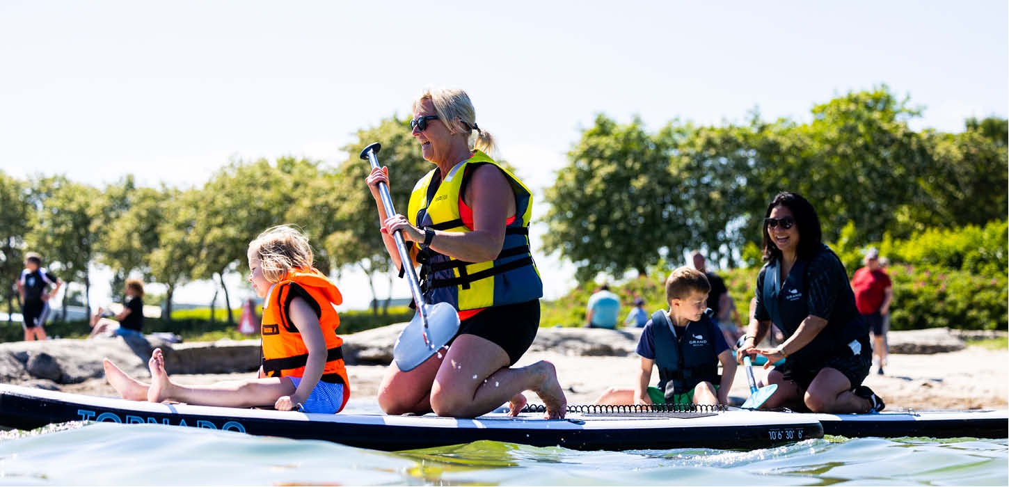 Kvinder og børn på supboards tæt på stranden ved Aarøsund