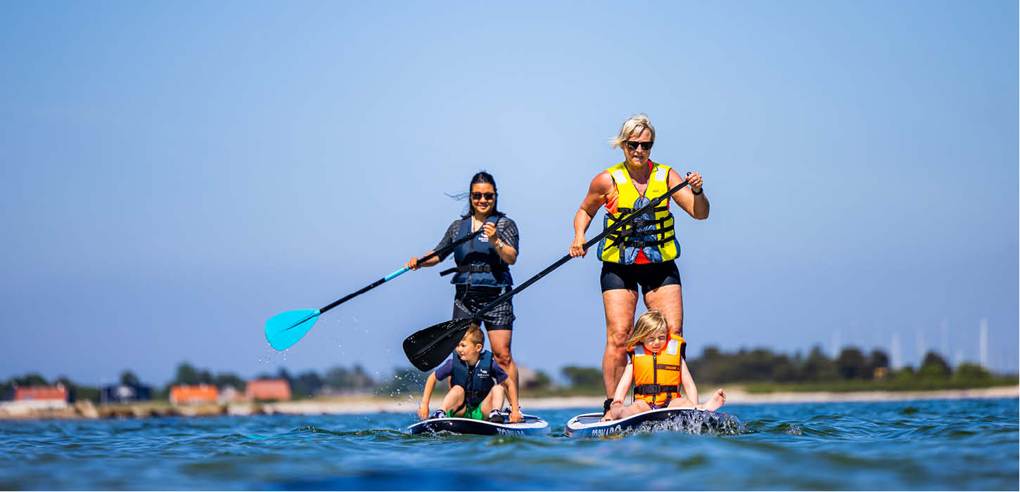 Kvinder og børn på supboards tæt på stranden ved Aarøsund